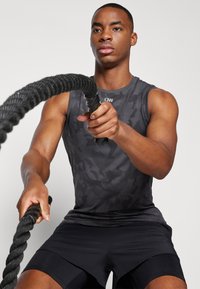 Svart kamuflasje tank topp og shorts, atletisk passform, holder et tykt svart treningstau, fokusert uttrykk, glatt tekstur, minimalistisk design.