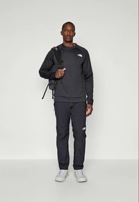Muška crna dukserica i hlače marke The North Face, izrađene od mekanog materijala. Dukserica ima logo na prednjoj strani; hlače imaju logo na bedru.