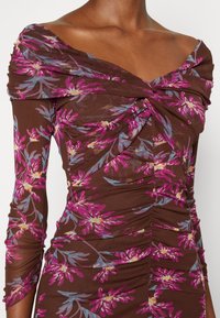 Top marrón oscuro con un diseño off-shoulder, que presenta patrones florales en púrpura y azul, y textura fruncida en las mangas y el cuerpo.