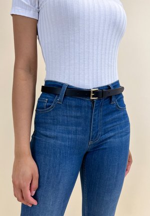 Black leather belt with a gold metal buckle worn over a fitted white ribbed top and blue jeans, highlighting a sleek, minimalist style.