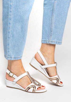 White wedge sandals featuring a curved design with metallic gold accents. The straps are adjustable, and the sole is textured for grip.