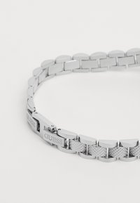 Sølvmetalarmbånd med sammenkoblede ovale led, teksturerede sektioner og en lås med prægede mærkelogo. Poleret finish.