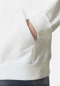 Sudadera blanca de algodón con un bolsillo frontal tipo canguro y puños acanalados. Presenta una textura suave y un corte casual, que se extiende en el dobladillo.