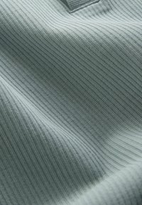 Világosszürke bordázott kötött anyag függőleges vonalakkal és finom redőkkel, valószínűleg egy ruhadarab gallérjának vagy nyakkivágásának része.