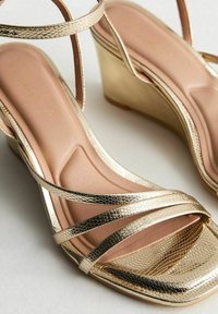 Sandalias cuña doradas con un patrón de piel de serpiente texturizado, finas correas cruzadas y una plantilla acolchada beige. Diseño elegante para un estilo elevado.
