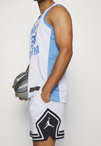 Tenue de basketball masculine composée d'un maillot sans manches blanc/menthe avec l'inscription "NORTH CAROLINA", assorti à un short blanc avec un logo Jordan noir.