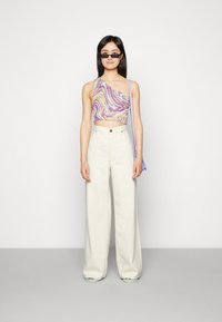 Top cropped em tons de roxo e amarelo em mármore, calças largas de cintura alta em creme e óculos de sol pretos elegantes. Inclui uma pequena mala lavanda.