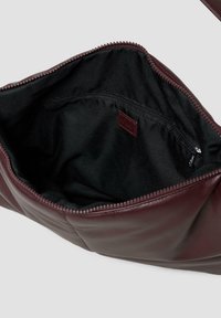 Bordeaux leren tas met een gladde textuur, voorzien van een ritsluiting en een zwart gevoerd interieur. Inclusief een kleinere ritszak aan de binnenkant.