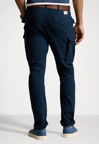 Navy blue cargo pants with side pockets and a textured finish, featuring a fitted silhouette and rolled cuffs, paired with blue sneakers.