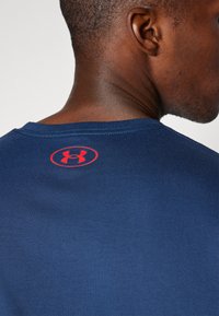 Mørkeblå bomulds T-shirt med rund halsudskæring, med et rødt Under Armour-logo på nakken og en glat, jævn tekstur.