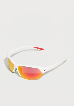 Športové slnečné okuliare s bielym rámom, červeným logom Nike a oranžovými zrkadlovými sklami, položené na bielom povrchu pod uhlom.