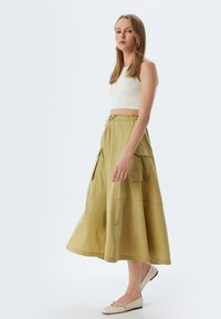 Olijfgroene, enkel-lange rok met een uitlopende ontwerp, een trekkoord tailleband en twee zijvakjes. Draag het met een wit cropped top en platte schoenen.