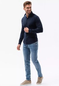 Camicia a maniche lunghe blu navy con colletto botton-down, design slim fit. Indossata con jeans blu chiaro e sneaker beige. Texture liscia.