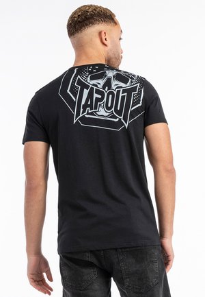 Crna majica s okruglim izrezom, s velikom bijelom lubanjom i ispisanim "TAPOUT" logotipom na leđima, izrađena od mekanog pamučnog materijala.