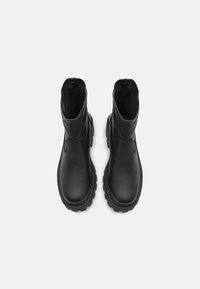 Des bottines en cuir noir présentent une surface lisse, un bout arrondi et une semelle en caoutchouc épaisse avec un motif texturé pour une meilleure adhérence.