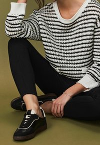 Black and white striped knit sweater with a ribbed neckline; paired with black leggings and black sneakers featuring white accents and brown soles.