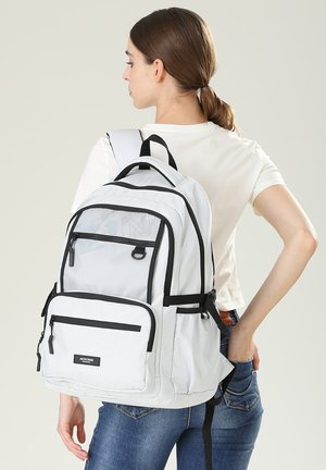Zaino bianco con dettagli neri, dotato di numerosi scomparti con zip, spallacci regolabili e una tasca frontale in rete. Progettato per la funzionalità.
