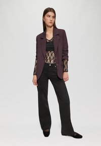 Lila strukturiertes Blazer über einem schwarzen Spitzenoberteil, kombiniert mit schwarzen weiten Jeans und schwarzen Ballerinas. Glatter Stoff mit taillierter Passform.