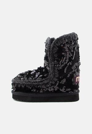 Botte de cheville noire à sequins avec une texture douce, bordure en fausse fourrure grise et semelle en caoutchouc plate. Présente des coutures décoratives et un patch logo.