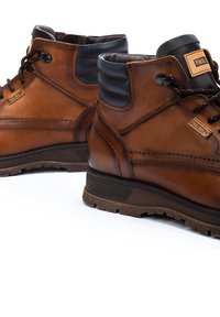 Bottes de cheville en cuir marron avec des accents noirs, présentant un dessus texturé, un design à lacets et une semelle en caoutchouc robuste. Détails de couture remarquables.