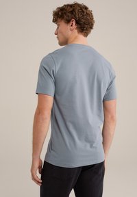 Camiseta de algodón de manga corta, azul claro, con cuello redondo y textura suave, combinada con pantalones oscuros, vista desde la espalda.