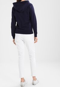 Sweat à capuche bleu marine à manches longues, en coton, avec poignets et ourlet côtelés, associé à un pantalon blanc ajusté et des baskets décontractées.