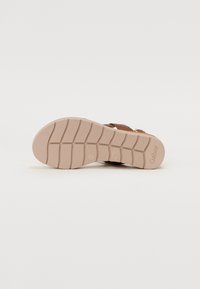 Brown sandal featuring a textured beige sole with a grip pattern and gold hardware accents. The footbed is contoured for comfort.