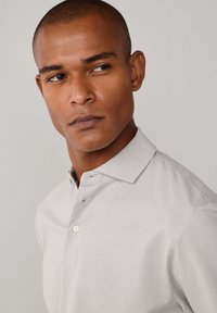 Polo gris con cuello, cierre de un solo botón y mangas cortas. Textura suave con un patrón sutil tejido. Diseño minimalista.