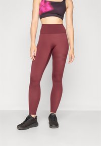 Bordeaux hoge taille leggings van rekbaar materiaal, met een gladde textuur en horizontale gestreepte accenten op de benen. Gecombineerd met zwarte schoenen.