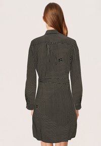 Vestito nero con strisce verticali in un motivo geometrico, maniche lunghe, polsini con bottoni e vita aderente con accenti sottili sul retro.