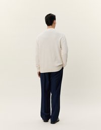 Maglione testurizzato bianco sporco con orlo a coste, abbinato a pantaloni larghi blu navy e scarpe nere, mostrato da dietro.