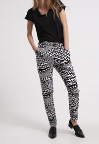 Black short-sleeved top paired with patterned black and white trousers featuring zigzag and geometric designs; black flat shoes.
