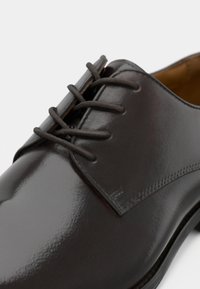 Tmavá kožená spoločenská obuv s hladkým, lesklým povrchom, zaoblenou špičkou a klasickým šnurovaním so štyrmi očkami.