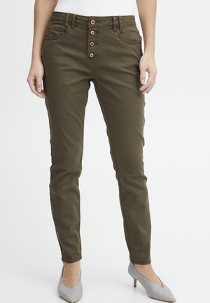 Olivgrüne, taillierte Jeans mit einem Fünf-Knopf-Verschluss, Seitentaschen und einer glatten Textur. Kombiniert mit hellgrauen High Heels.