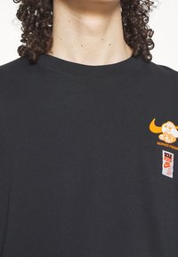 Black cotton T-shirt featuring an orange graphic with a cartoonish food character and two printed tags, one labeled "Sole Food" and "Nike."