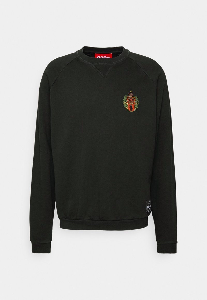 Sweat-shirt noir col rond à manches longues, petit blason brodé sur la poitrine gauche, et un patch rectangulaire noir et blanc près de l'ourlet.