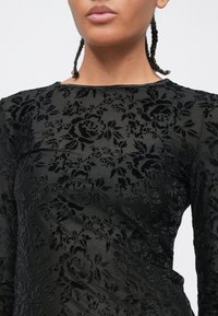 Schwarzes Samtkleid mit floralem Muster, das eine strukturierte, erhabene Darstellung von Rosen und Blättern zeigt, mit rundem Ausschnitt und langen Ärmeln.