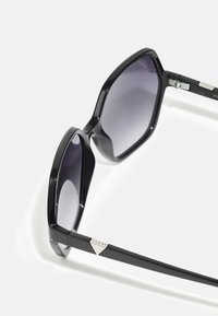 Black sunglasses with a wide, angular frame and gradient gray lenses. Features branded silver accents on the temple. Smooth, glossy finish.