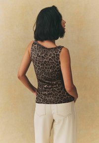 Kohvi leopardimustriga tank top, mis on valmistatud sileda kangaga, omab varrukateta disaini ja ümarat kaelust, koos heledate valgete pükstega.