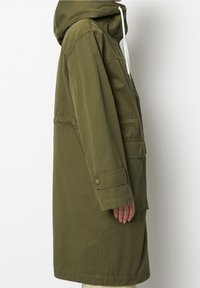 Olivgrön, knä-lång parka jacka gjord av ett mjukt, lättviktigt material. Har en huva, framsidans fickor och justerbara ärmslut med tryckknappar.