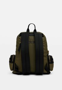 Zaino verde oliva con spallacci neri, dotato di una tasca con zip sul retro e tasche laterali, realizzato in tessuto resistente con un design elegante.