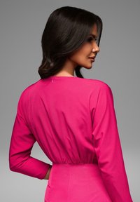 Fuksia kangasmekko pitkähihaisilla, vartalonmyötäisellä vyötäröllä ja takavetoketjulla. Sujuva texture ja minimalistinen muotoilu.