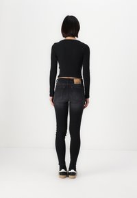 Černý top s dlouhým rukávem je kombinován s tmavě gradientními skinny džínami. Džíny mají na zadním pásu označení z hnědé kůže.
