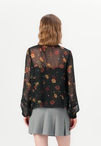 Blusa nera floreale realizzata in tessuto trasparente con maniche lunghe, caratterizzata da vari fiori colorati e un motivo a pois texture.