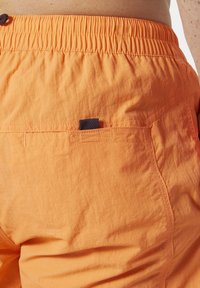 Oranžové šortky s elastickým pasem, zadní kapsou s námořnickým akcentem a lehkým, strukturovaným materiálem.