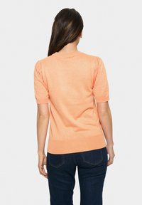 Maglione corto a maniche corte color pesca con scollo rotondo e orlo a coste. Il retro presenta un tessuto morbido e sottili dettagli a sbuffo sulle maniche.