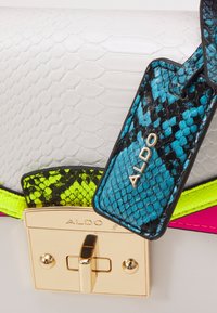 Borsa bianca in pelle di serpente con fermaglio dorato, con tracolla multicolore in verde neon e rosa, e targhetta turchese con motivo a serpente.
