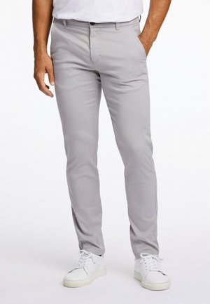 Pantalons gris clair en tissu lisse, avec une coupe slim, des poches avant et une taille standard avec une fermeture à bouton. Portés avec des baskets blanches.