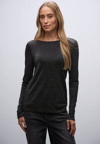 Zwarte lange mouwen top met een ronde hals, gemaakt van een sprankelende textuur, gecombineerd met donkere jeans, weergegeven tegen een neutrale achtergrond.