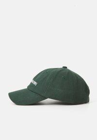 Green baseball cap made of fabric with a curved brim, featuring embroidered text on the front and ventilation holes on the sides.